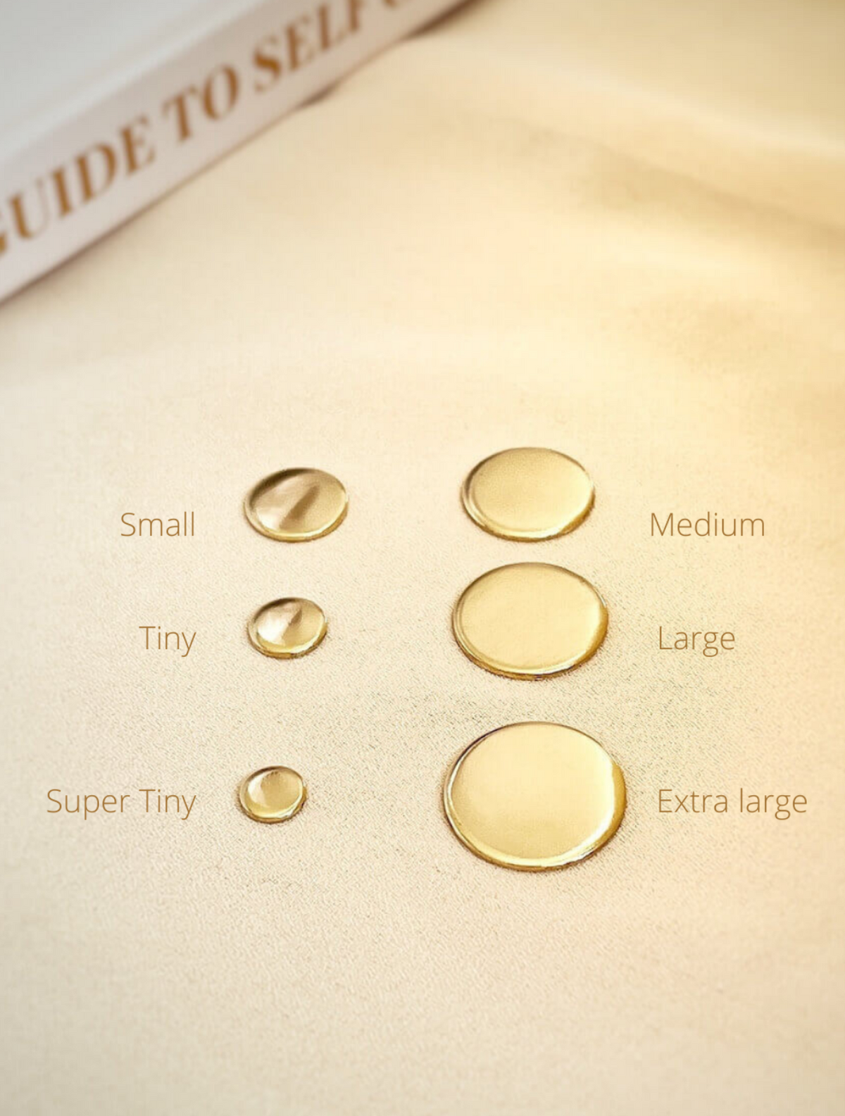 A series of four gold-colored pendants in different sizes displayed on a beige surface, labeled as small, medium, super tiny, and extra large.