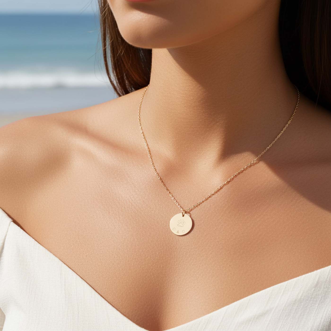Close-up of a person wearing a gold necklace with a beach in the background