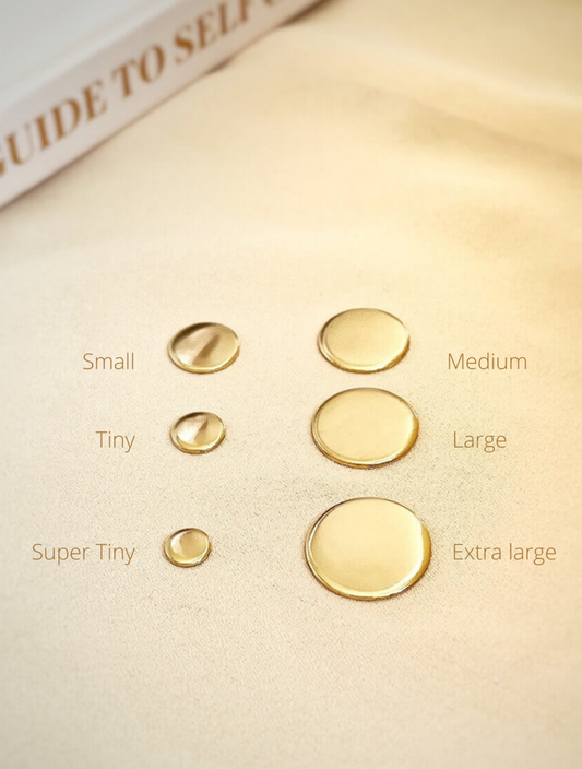 A series of four gold-colored pendants in different sizes displayed on a beige surface, labeled as small, medium, super tiny, and extra large.